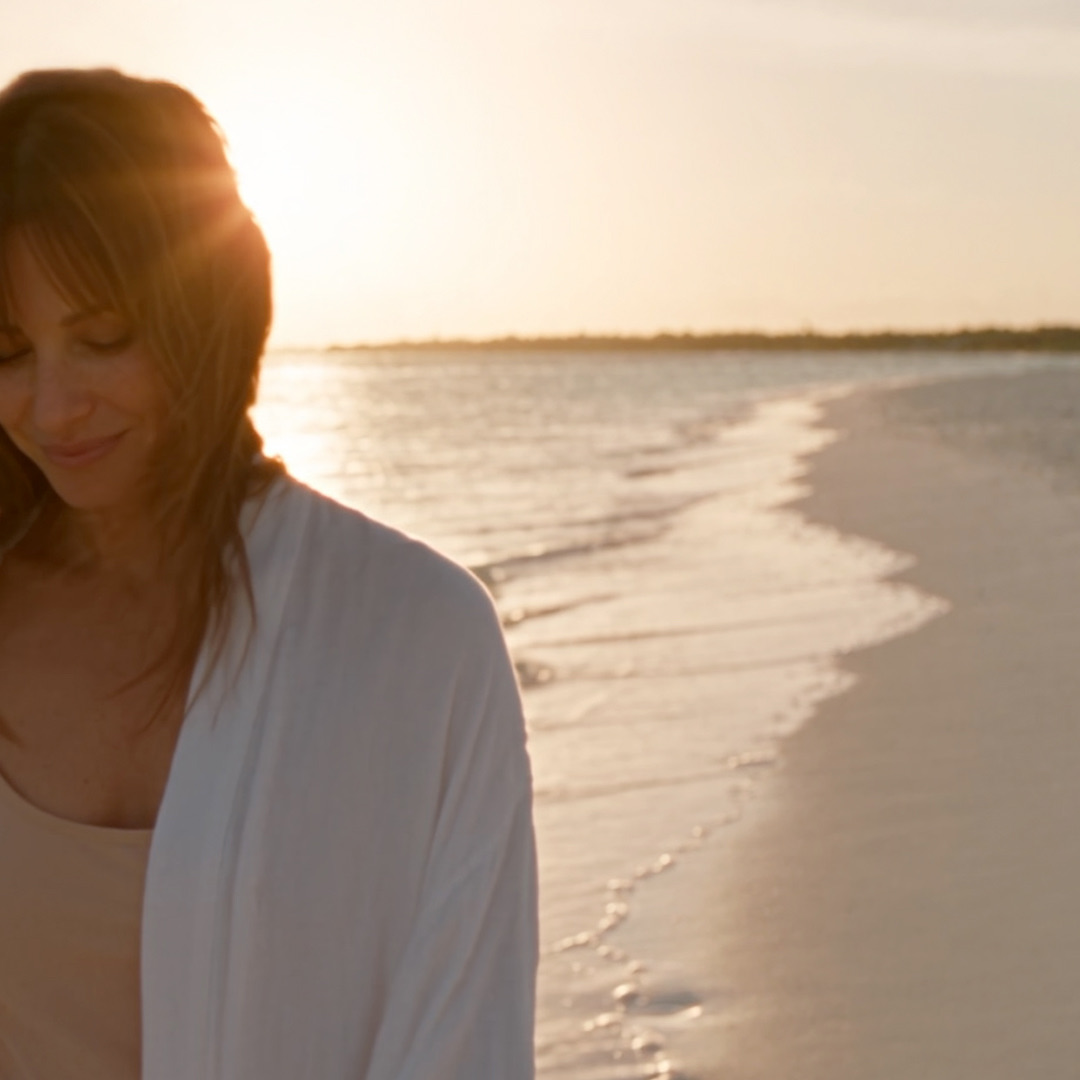 A guest smiling on a beach at sunset